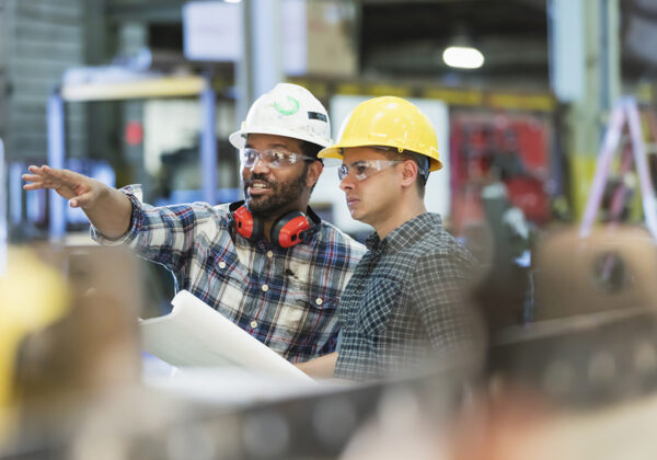 two construction workers in protective equipment talk about a project